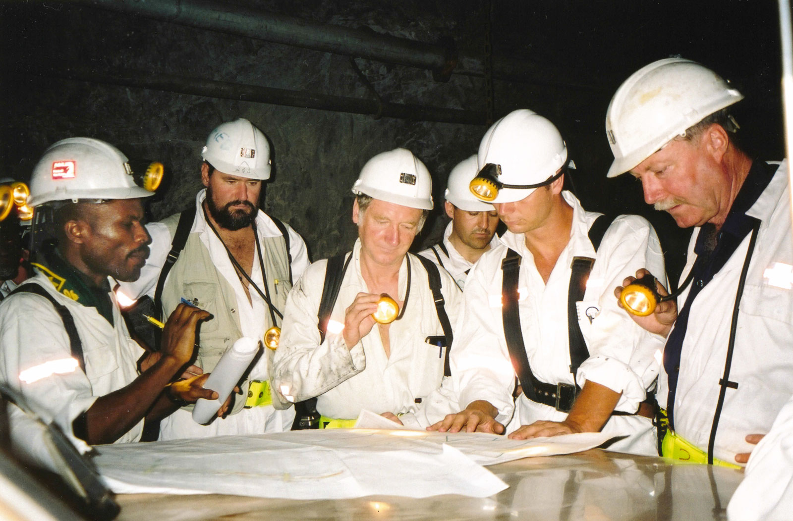 [Ashanti Goldfields staff explain the orebody over plans on a Toyota bonnet, underground at Obuasi, Ghana.]